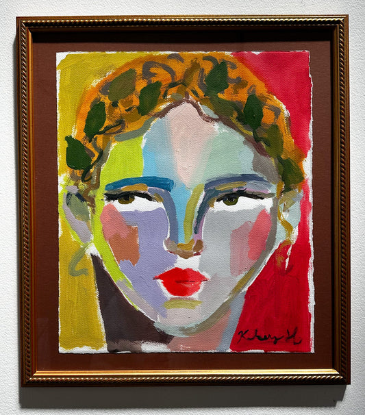 Colorful abstract painting of a face with a gold frame on a white wall